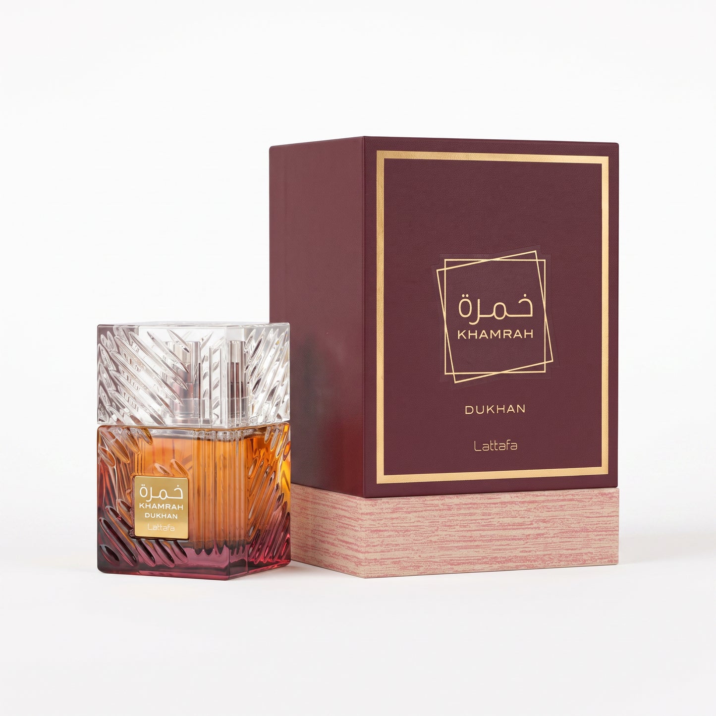 A bottle of Lattafa Dukhan perfume with amber liquid and a textured silver cap, displayed next to its dark burgundy and gold outer packaging box on a white background.